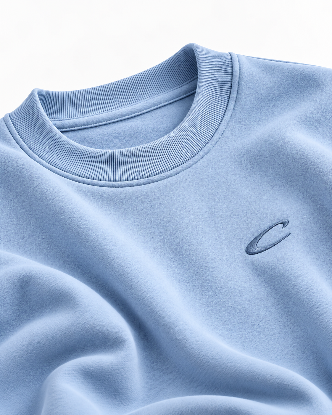 Close-up of the Calcuera Icon Sweatshirt in sky blue showing the ribbed collar and tonal embroidered C emblem